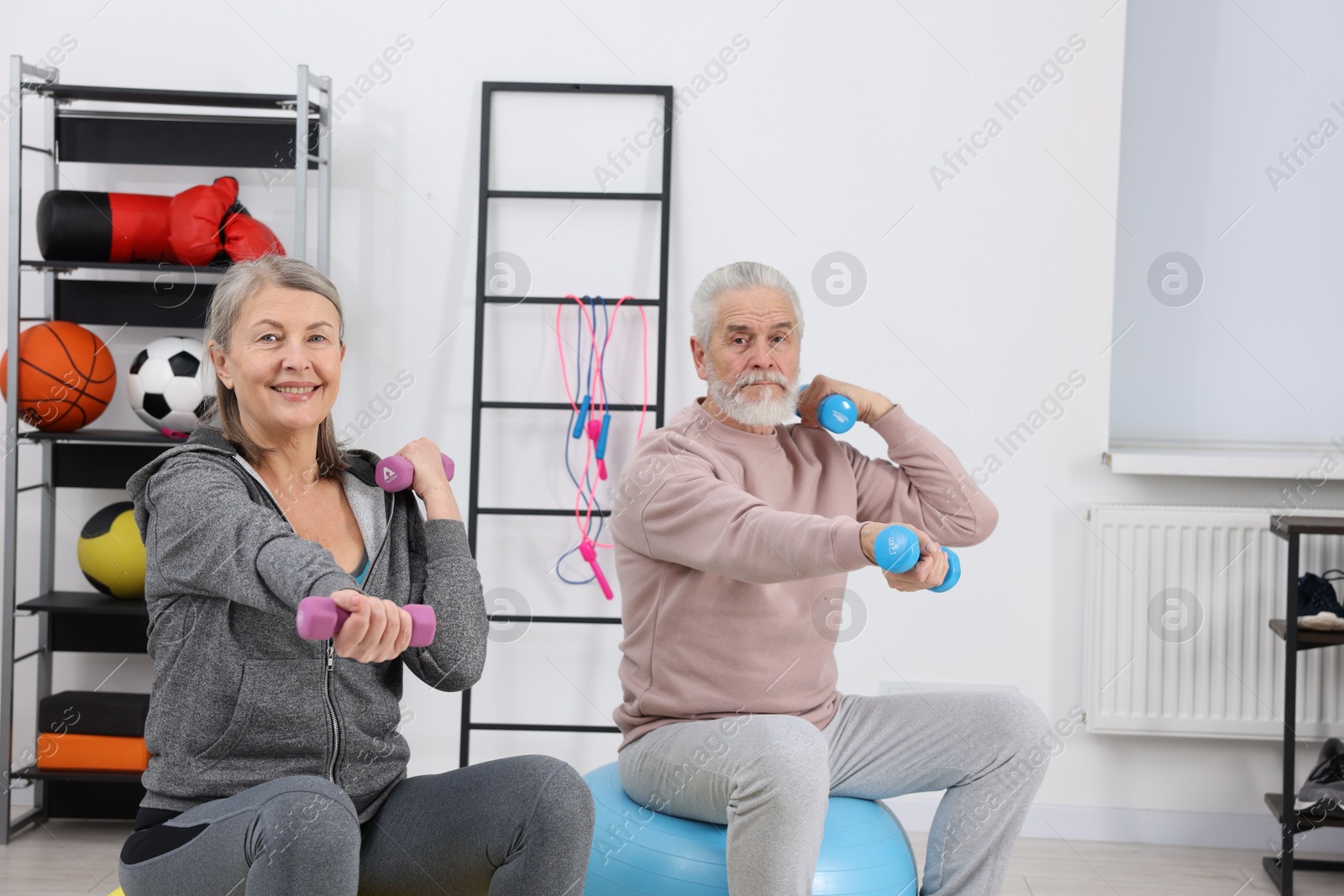 Photo of Elderly couple exercising with dumbbells and fitness balls at home