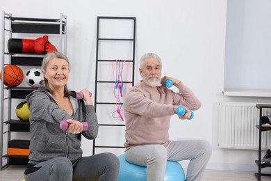 Photo of Elderly couple exercising with dumbbells and fitness balls at home