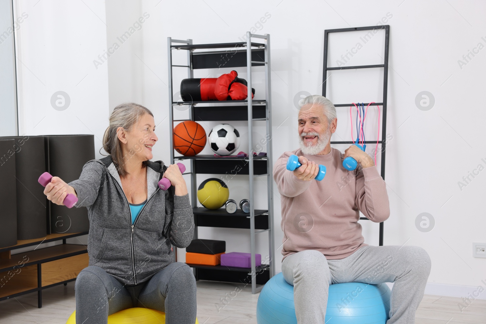 Photo of Smiling elderly couple exercising with dumbbells and fitness balls at home