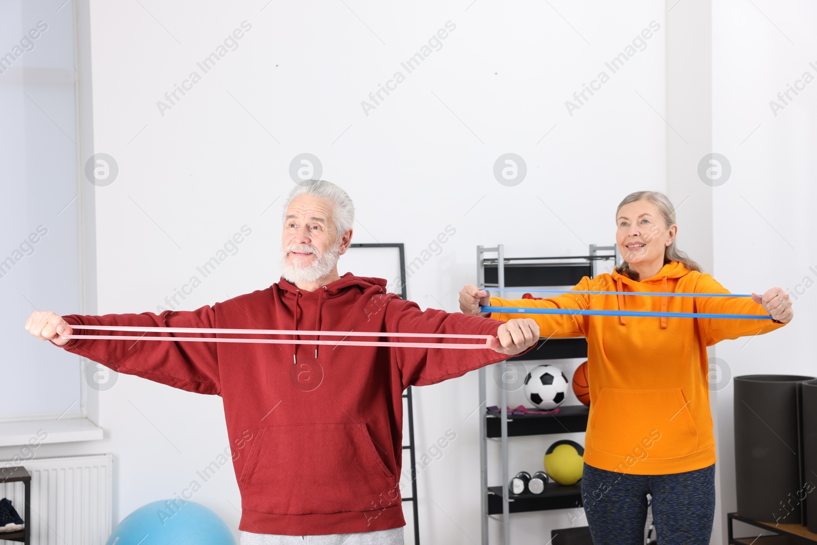 Photo of Smiling elderly couple exercising with fitness elastic bands at home