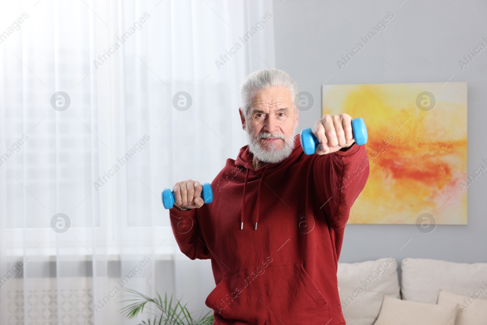 Photo of Elderly man exercising with dumbbells at home