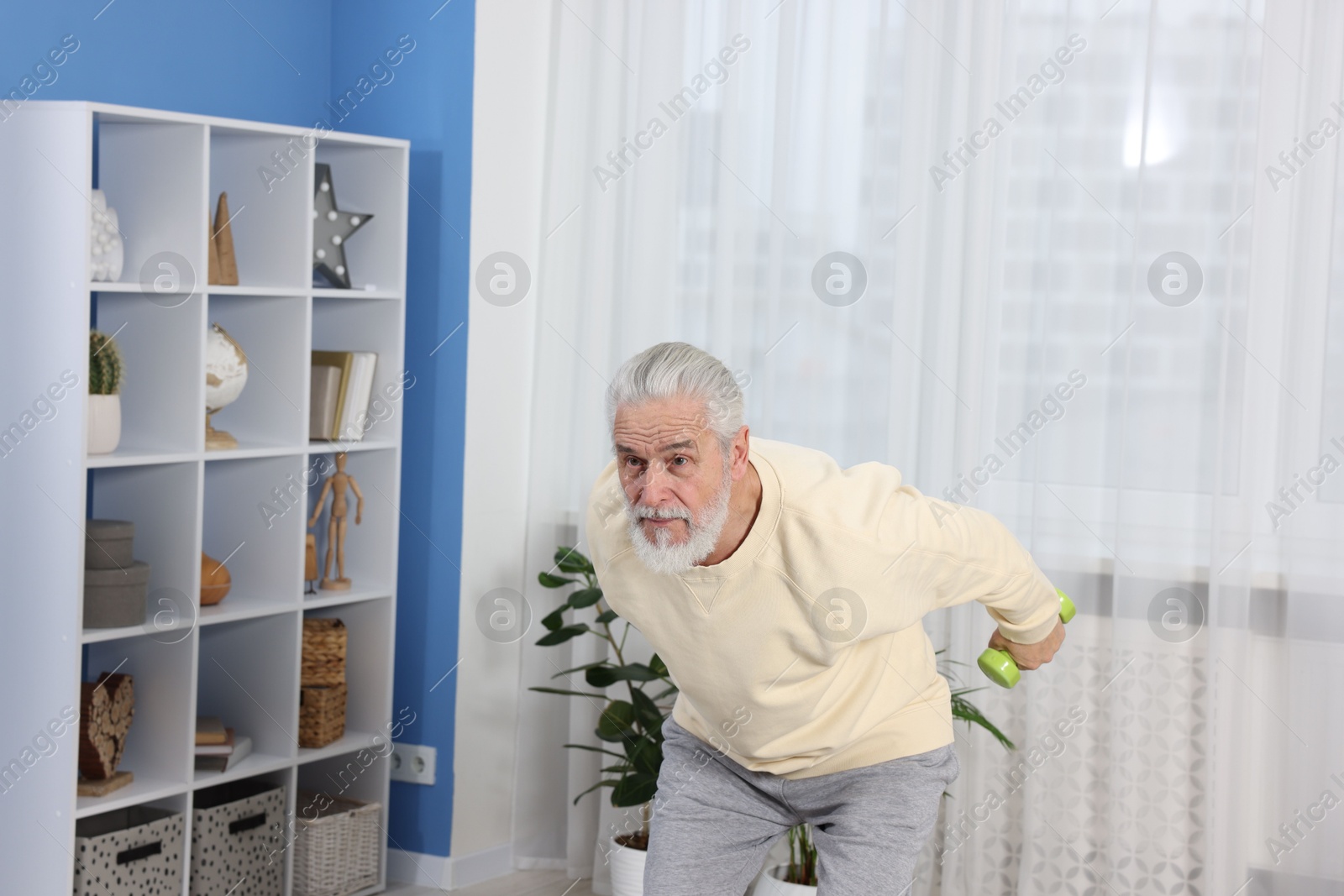 Photo of Elderly man exercising with dumbbells at home