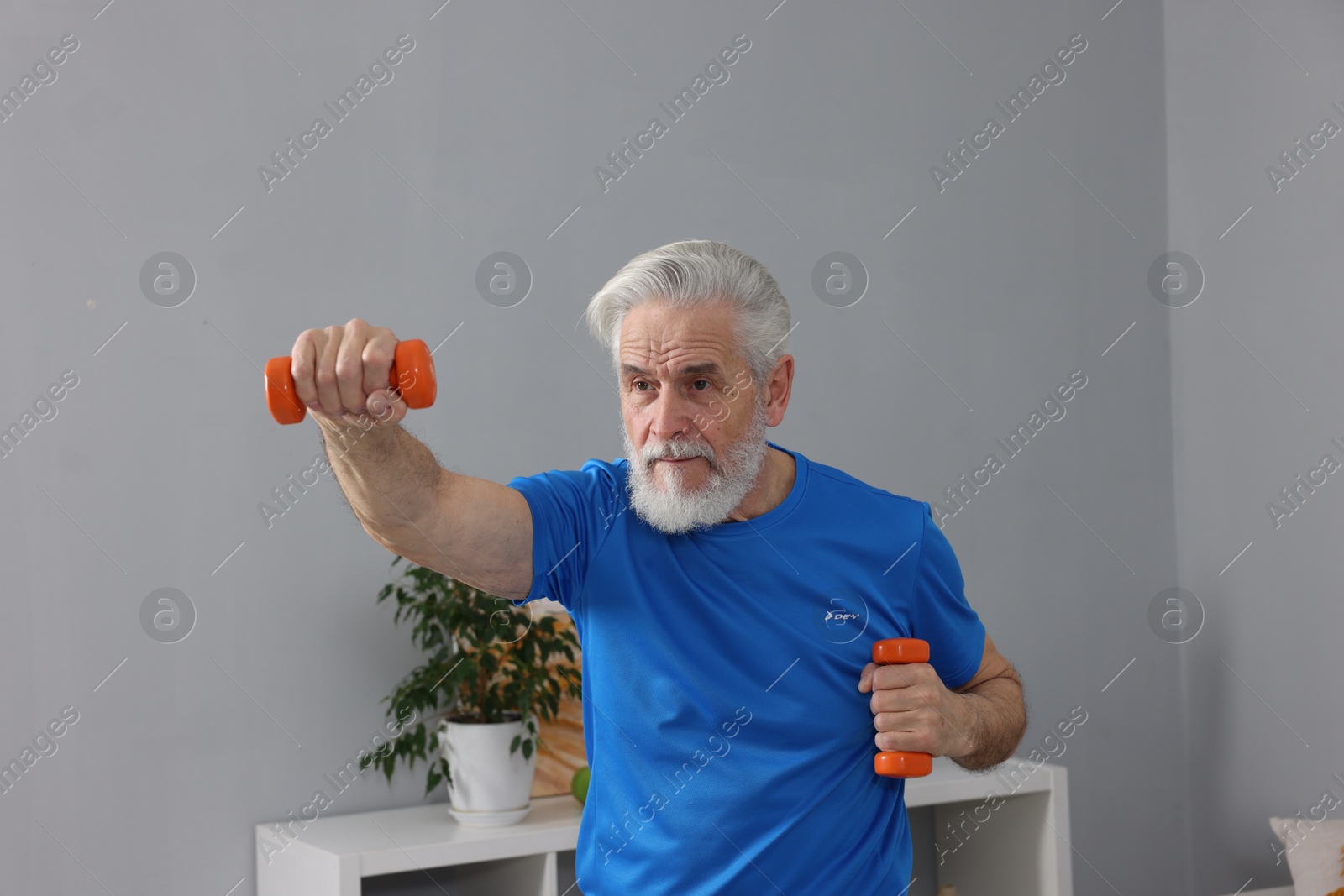 Photo of Elderly man exercising with dumbbells at home