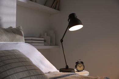 Photo of Glowing night lamp and alarm clock on bedside table indoors