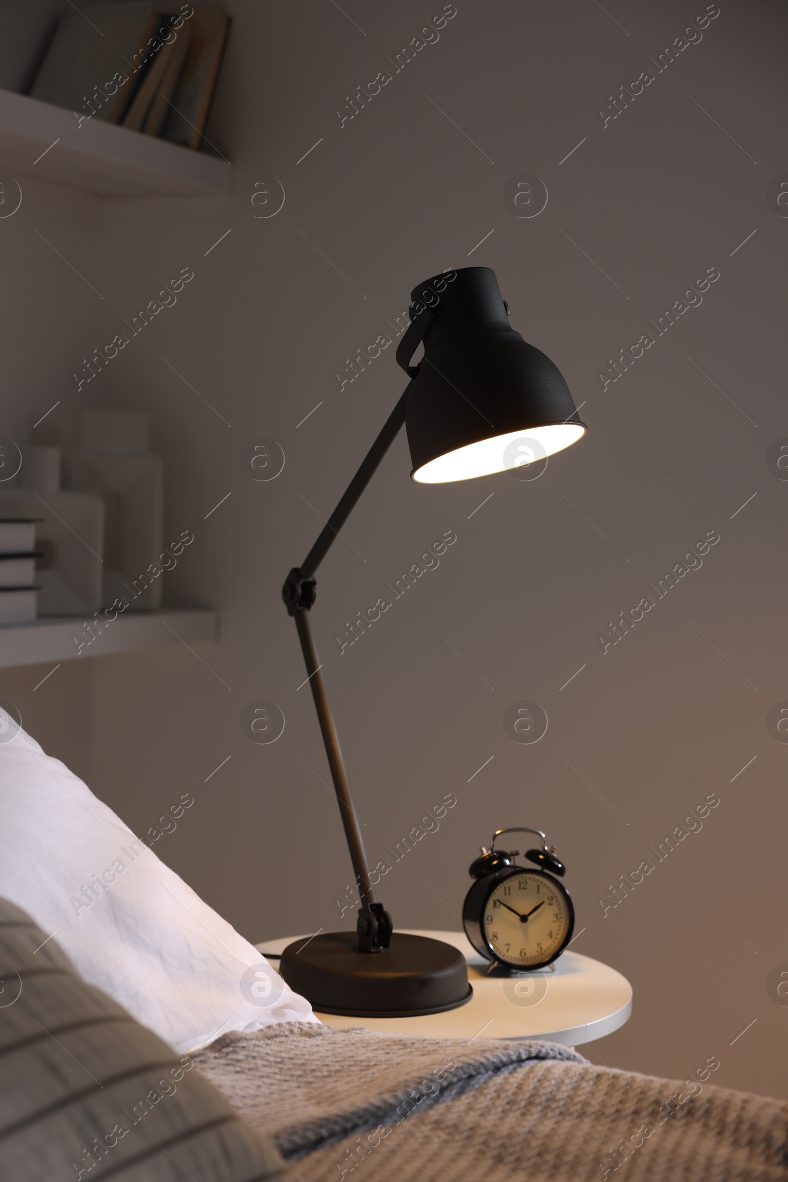 Photo of Glowing night lamp and alarm clock on bedside table indoors