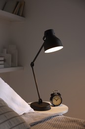 Photo of Glowing night lamp and alarm clock on bedside table indoors