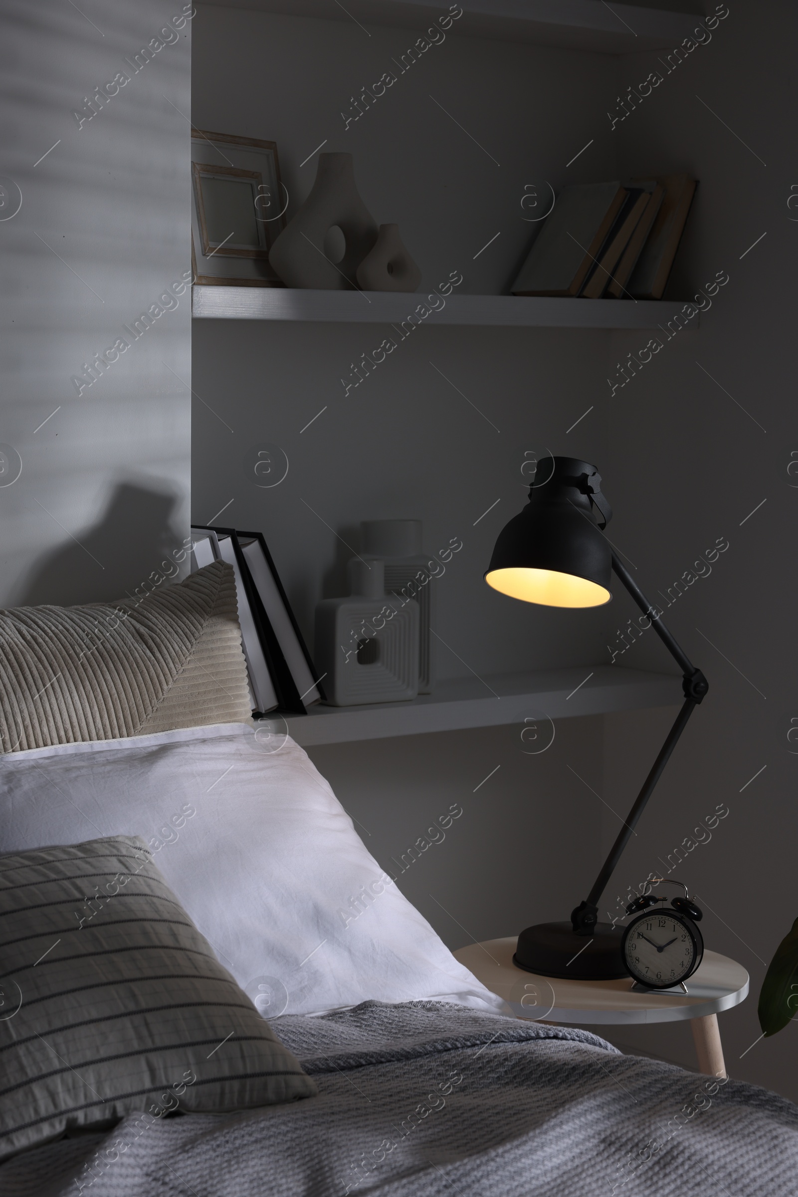 Photo of Glowing night lamp and alarm clock on bedside table indoors