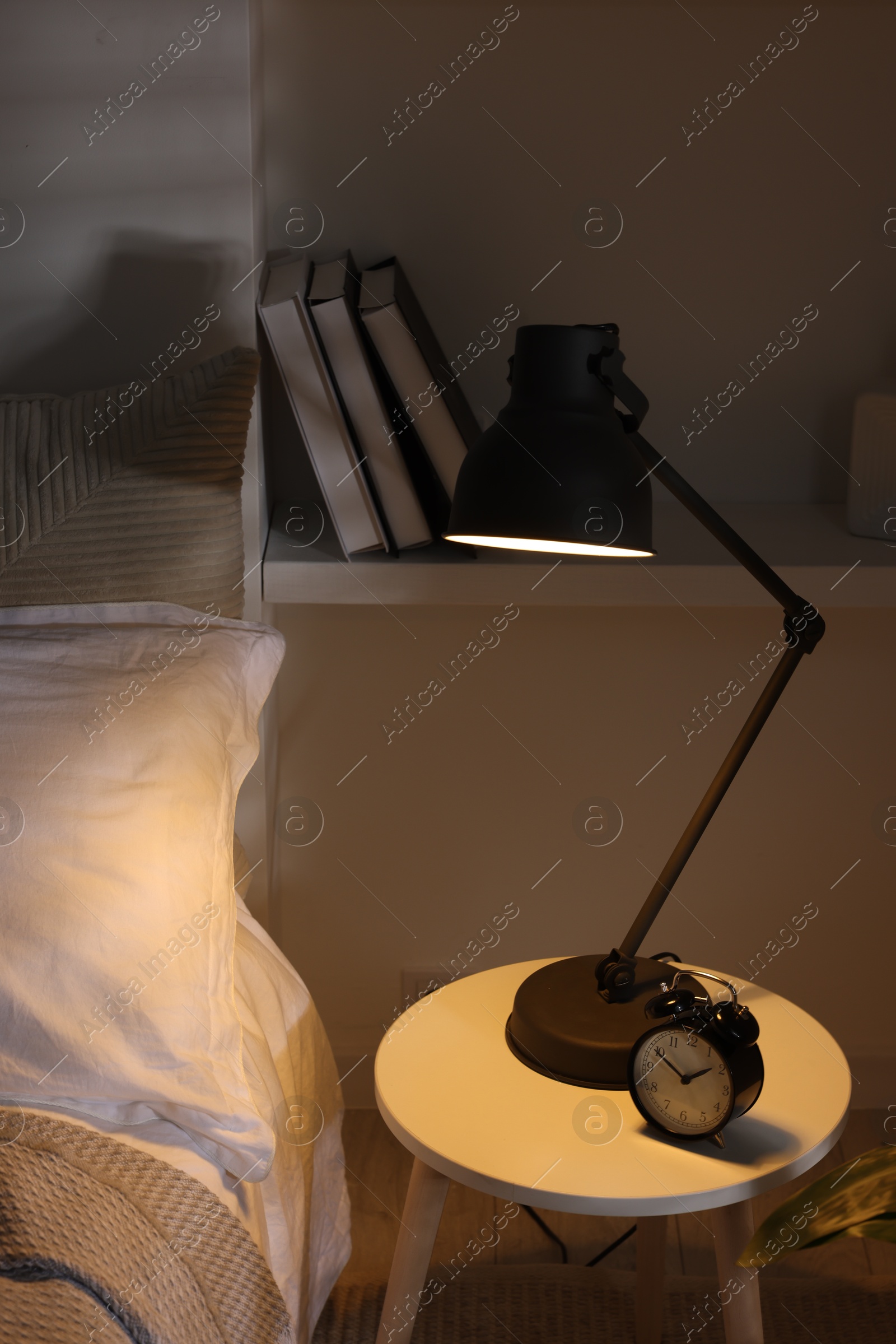 Photo of Glowing night lamp and alarm clock on bedside table indoors