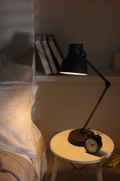 Photo of Glowing night lamp and alarm clock on bedside table indoors