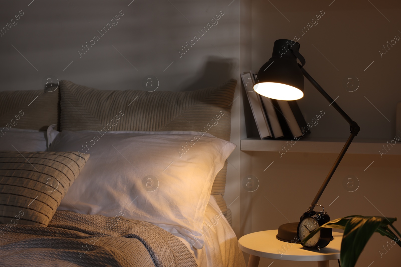 Photo of Glowing night lamp and alarm clock on bedside table indoors