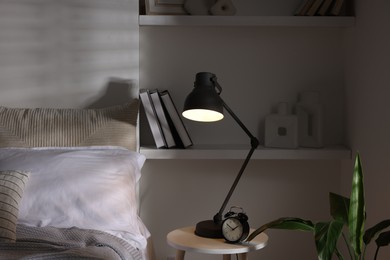 Photo of Glowing night lamp and alarm clock on bedside table indoors