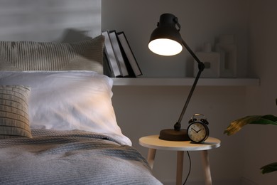 Photo of Glowing night lamp and alarm clock on bedside table indoors