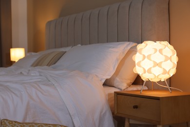 Photo of Glowing lamp on nightstand near bed indoors