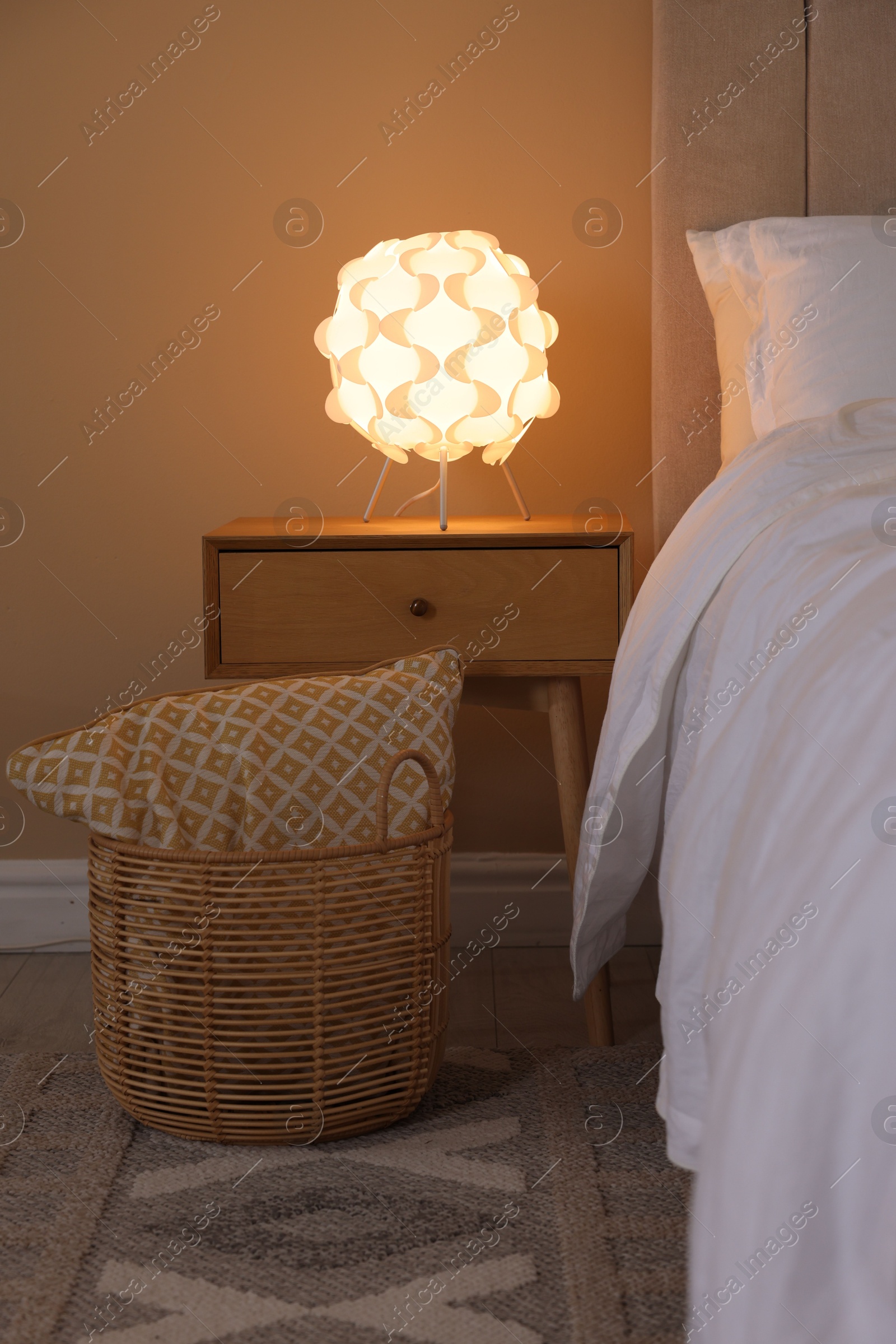 Photo of Glowing lamp on nightstand near bed indoors