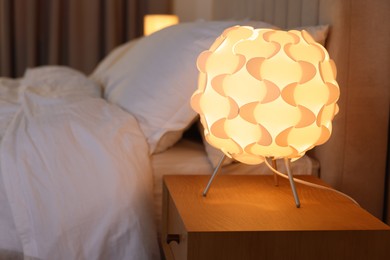 Photo of Glowing lamp on nightstand near bed indoors