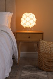 Photo of Glowing lamp on nightstand near bed indoors