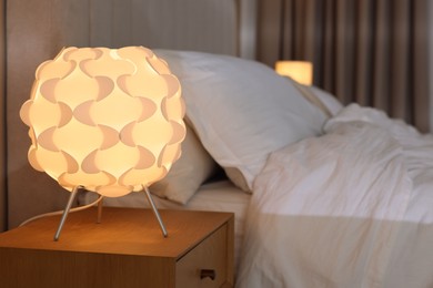 Photo of Glowing lamp on nightstand near bed indoors