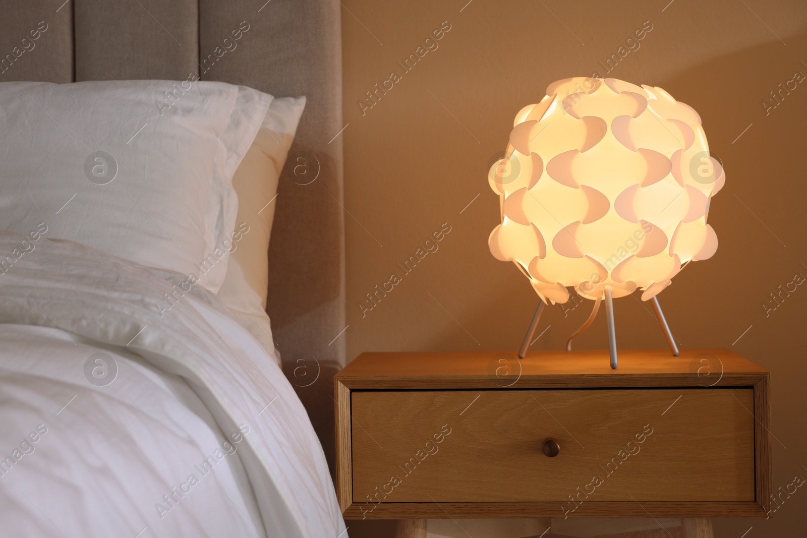 Photo of Glowing lamp on nightstand near bed indoors