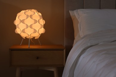 Photo of Glowing lamp on nightstand near bed indoors