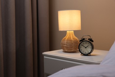 Photo of Glowing lamp and alarm clock on nightstand in bedroom. Space for text