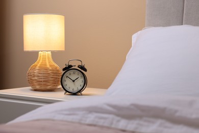 Photo of Glowing lamp and alarm clock on nightstand in bedroom