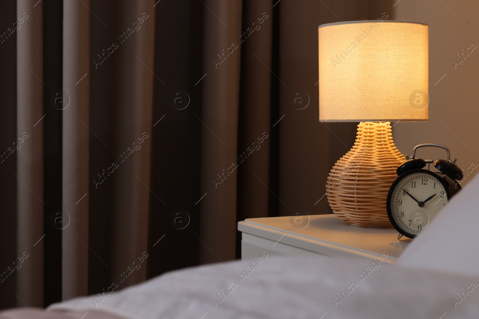 Photo of Glowing lamp and alarm clock on nightstand in bedroom. Space for text