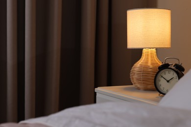 Photo of Glowing lamp and alarm clock on nightstand in bedroom. Space for text