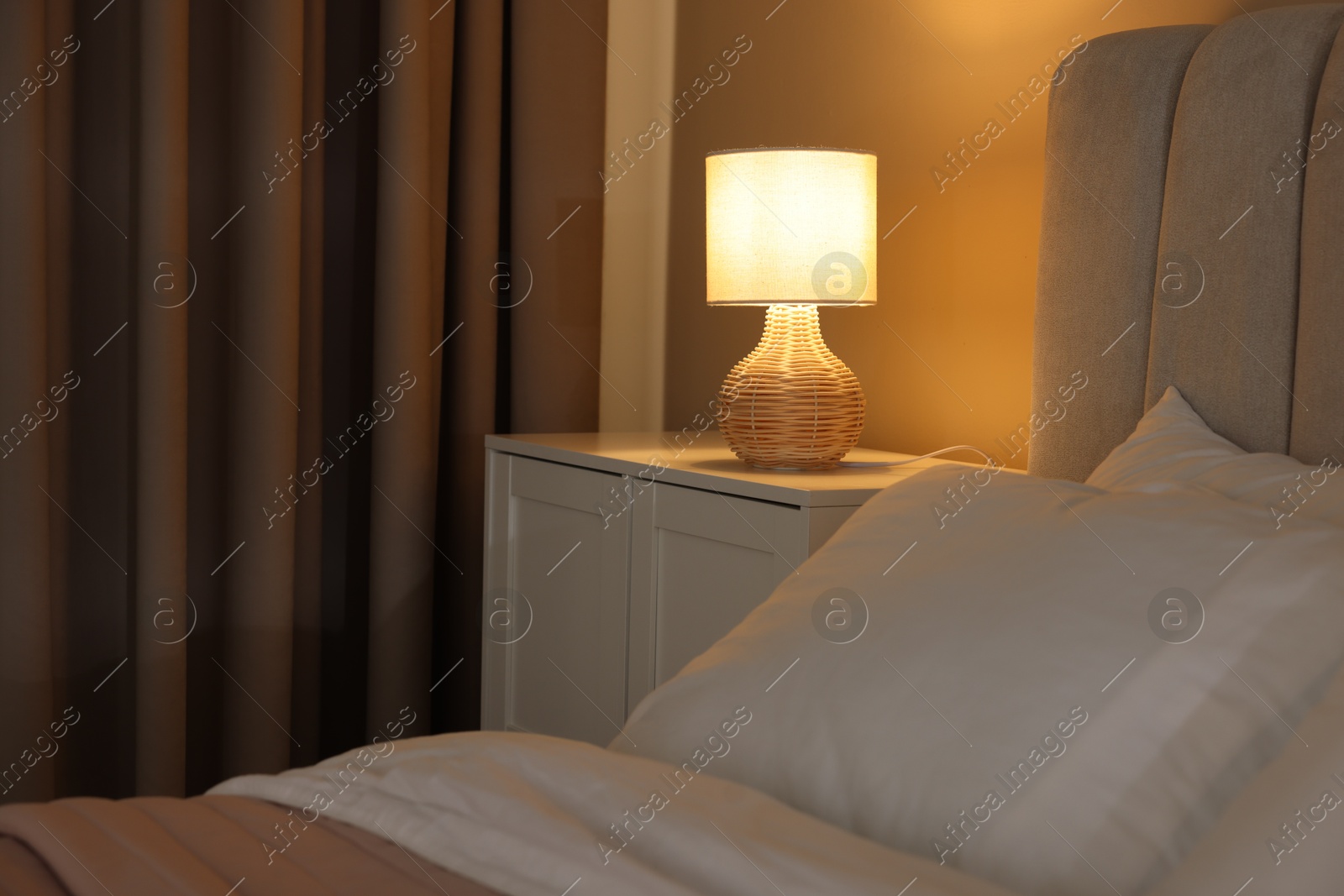 Photo of Glowing lamp on nightstand in bedroom. Space for text