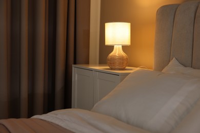 Photo of Glowing lamp on nightstand in bedroom. Space for text