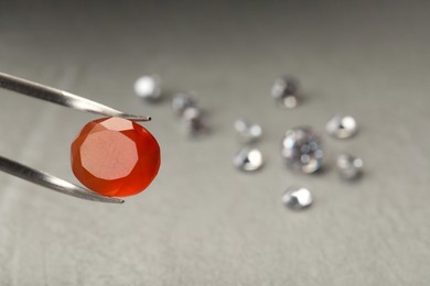 Photo of Tweezers with beautiful gemstone on blurred background, closeup