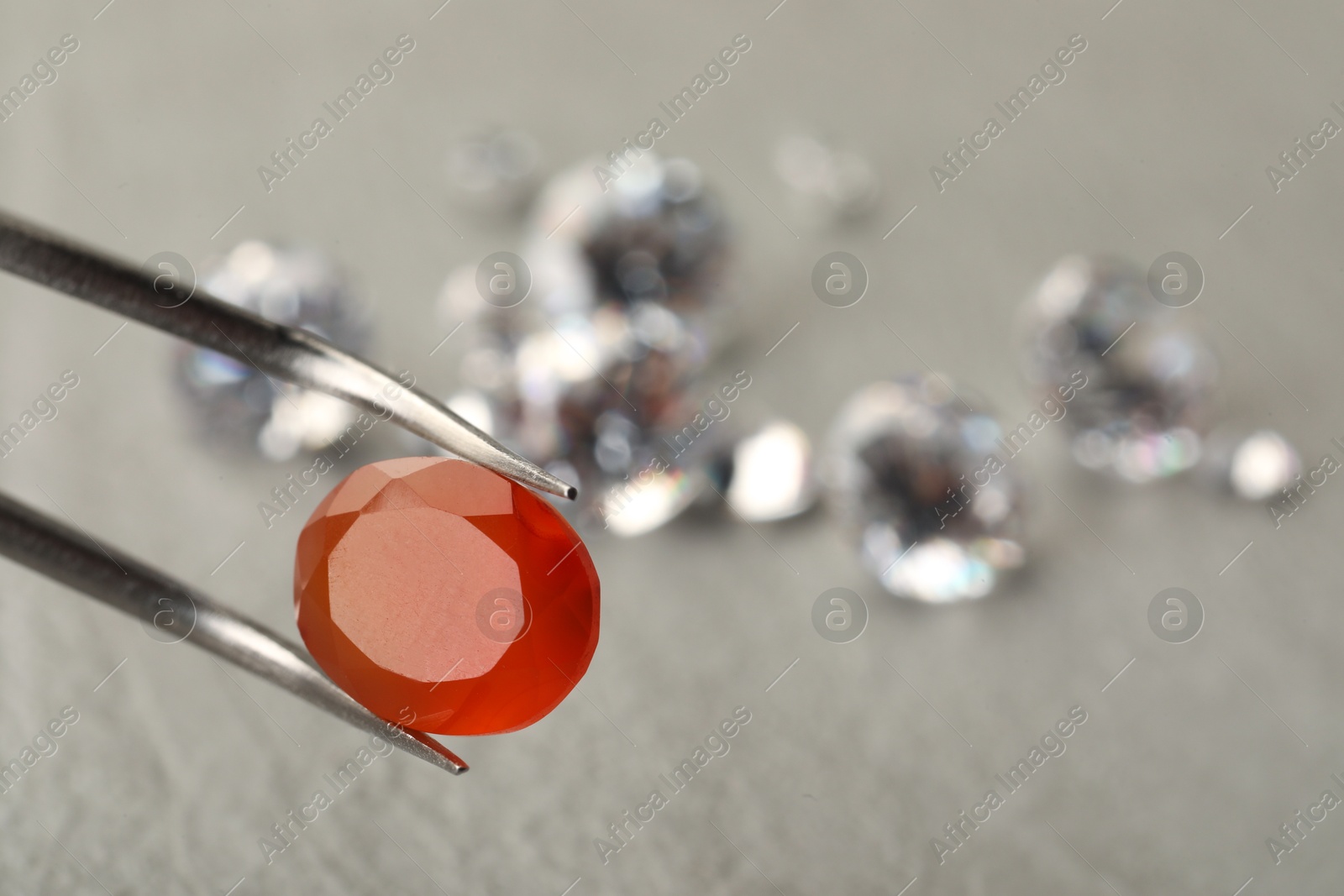 Photo of Tweezers with beautiful gemstone on blurred background, closeup