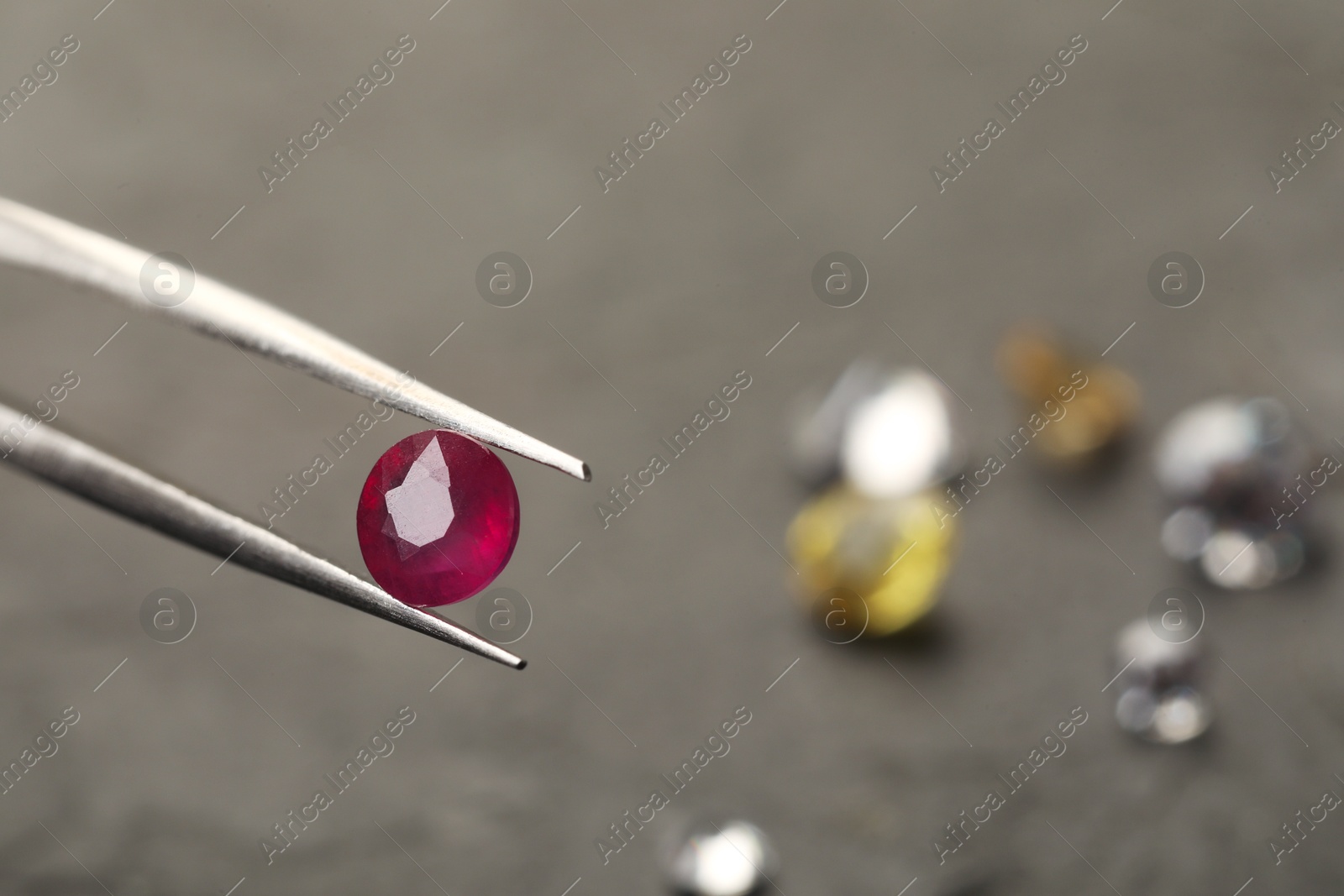 Photo of Tweezers with beautiful gemstone on blurred background, closeup