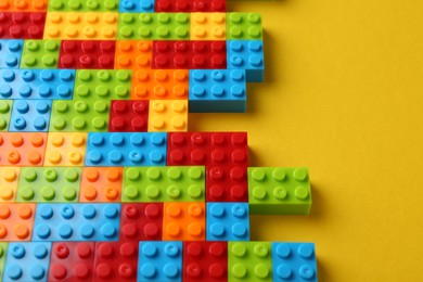 Photo of Constructor toy. Many colorful building blocks on yellow background, above view. Space for text