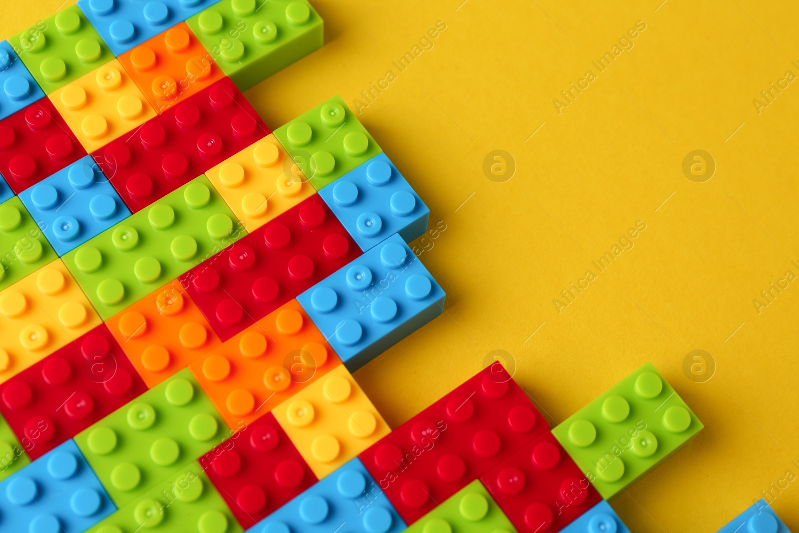 Photo of Constructor toy. Many colorful building blocks on yellow background, above view. Space for text