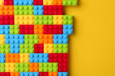 Photo of Constructor toy. Many colorful building blocks on yellow background, top view. Space for text