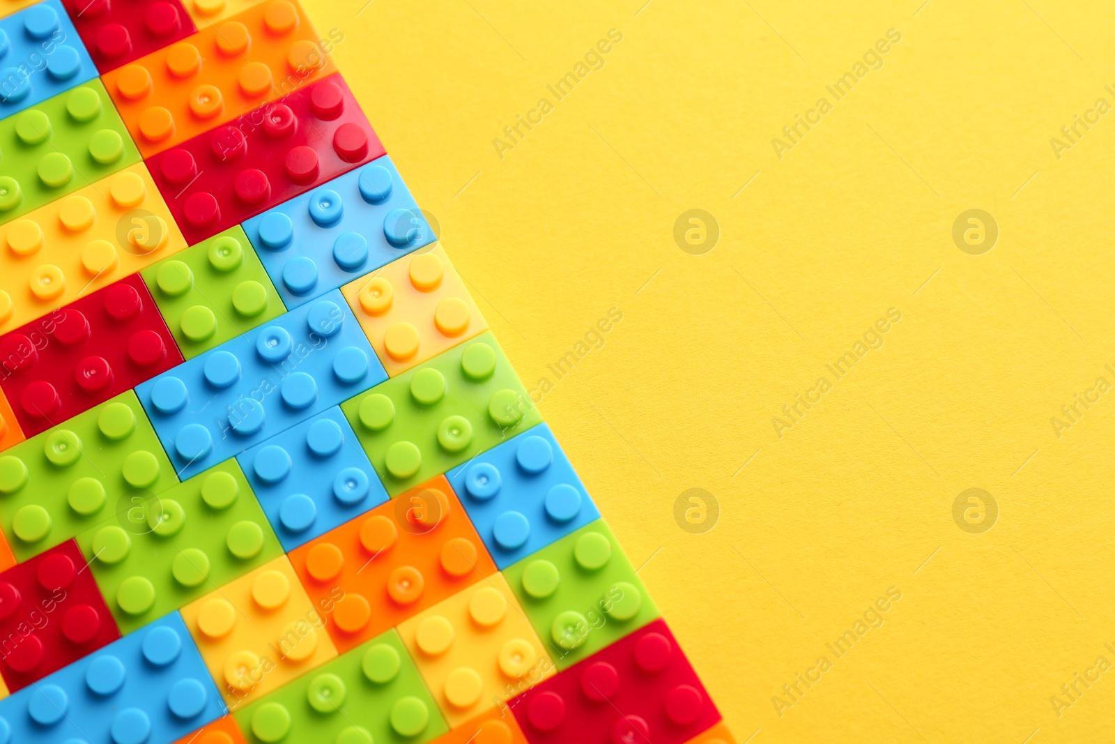 Photo of Constructor toy. Many colorful building blocks on yellow background, top view. Space for text