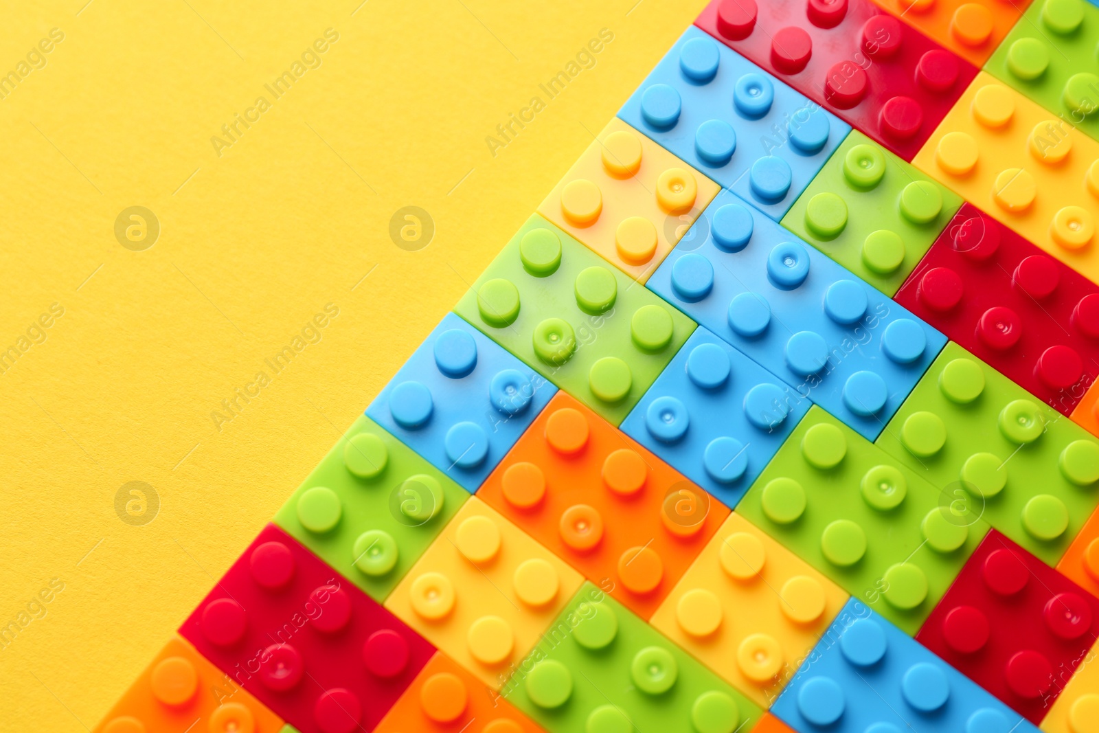 Photo of Constructor toy. Many colorful building blocks on yellow background, top view. Space for text