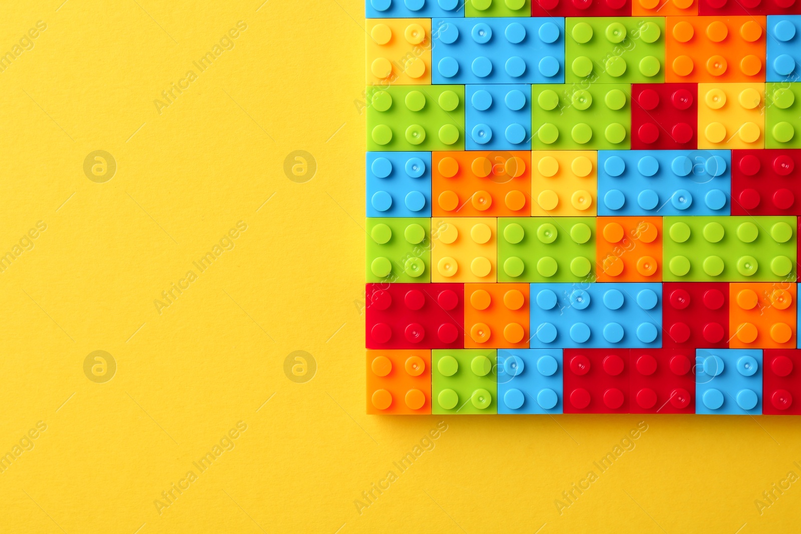 Photo of Constructor toy. Many colorful building blocks on yellow background, top view. Space for text