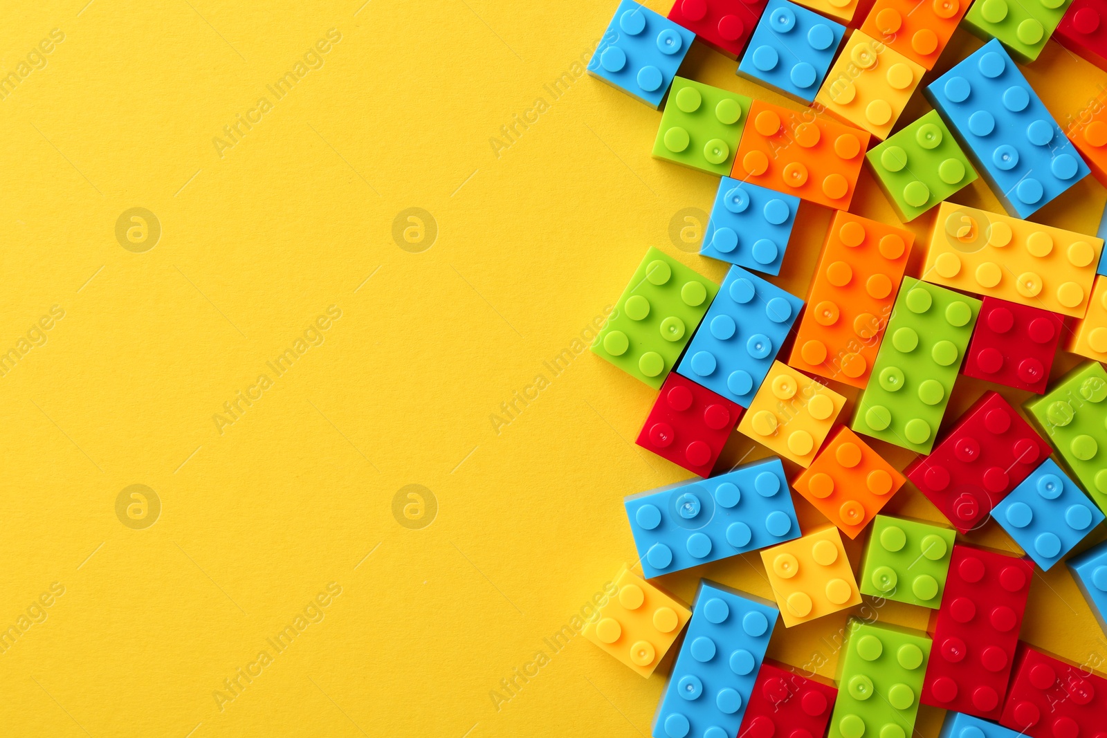 Photo of Constructor toy. Many colorful building blocks on yellow background, flat lay. Space for text