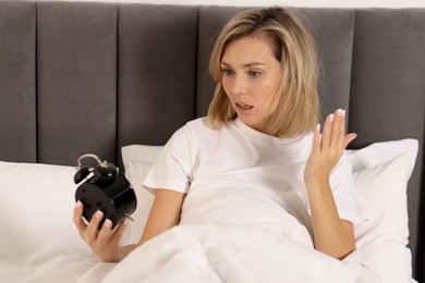 Photo of Overslept woman with alarm clock in bed at home