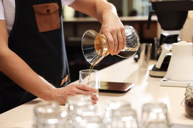 Photo of Barista pouring coffee from glass coffeemaker into cup at table in cafe, closeup