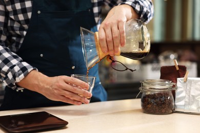 Photo of Barista pouring coffee from glass coffeemaker into cup at table in cafe, closeup