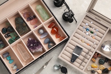 Photo of Box with beautiful gemstones and jeweler's tools on light table, closeup