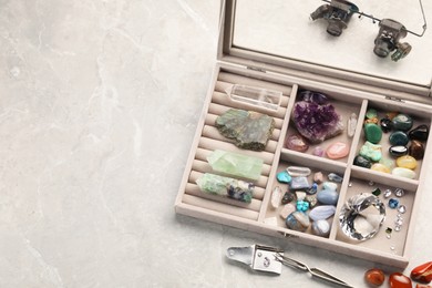 Photo of Box with beautiful gemstones and jeweler's tools on light table, above view. Space for text