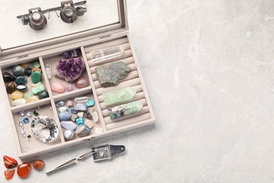 Photo of Box with beautiful gemstones and jeweler's tools on light table, above view. Space for text