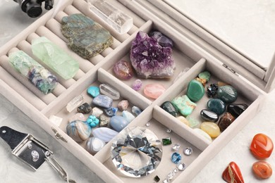 Photo of Box with beautiful gemstones and jeweler's tools on light table, closeup