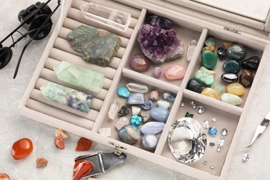 Photo of Box with beautiful gemstones and jeweler's tools on light table, closeup