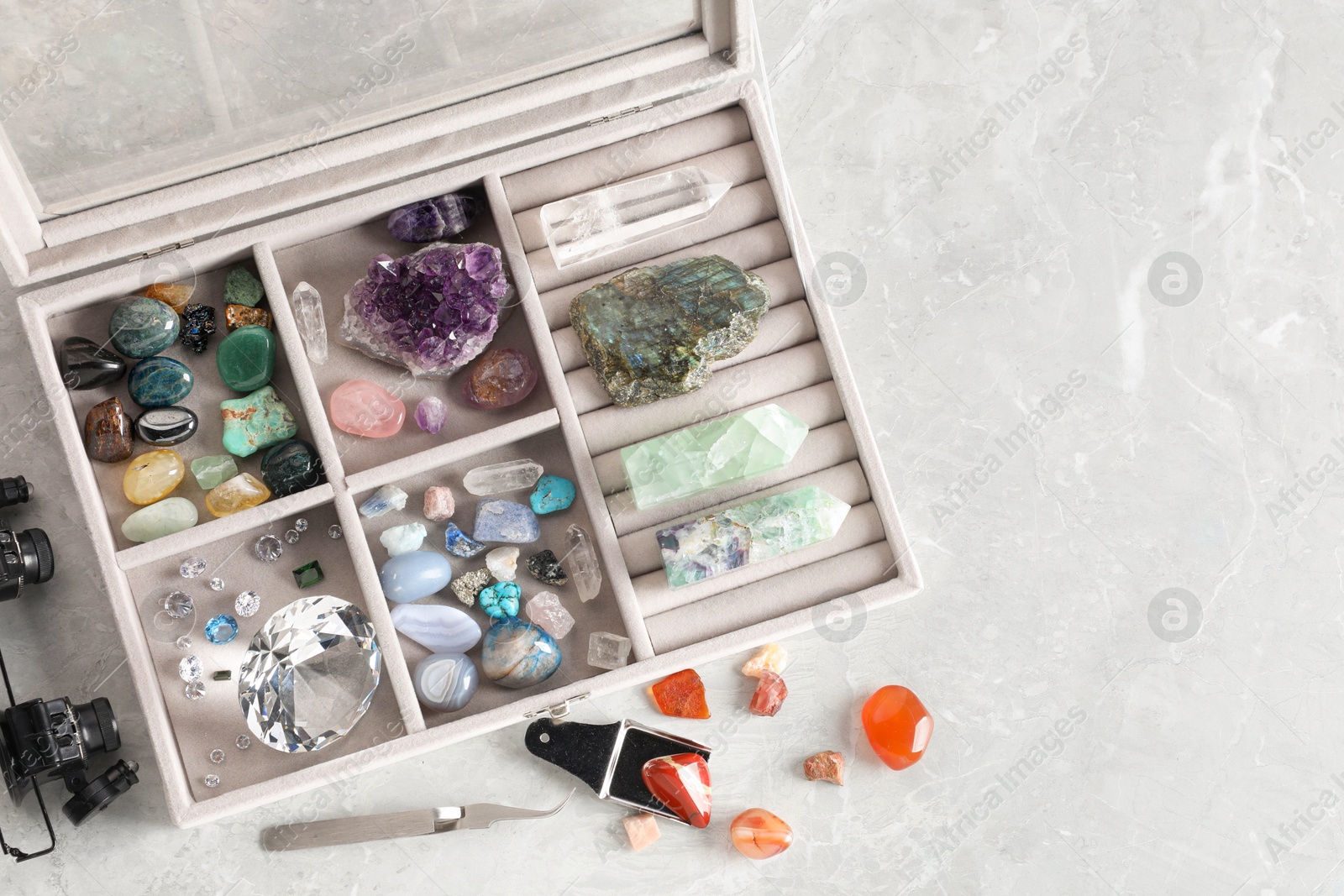 Photo of Box with beautiful gemstones and jeweler's tools on light table, flat lay