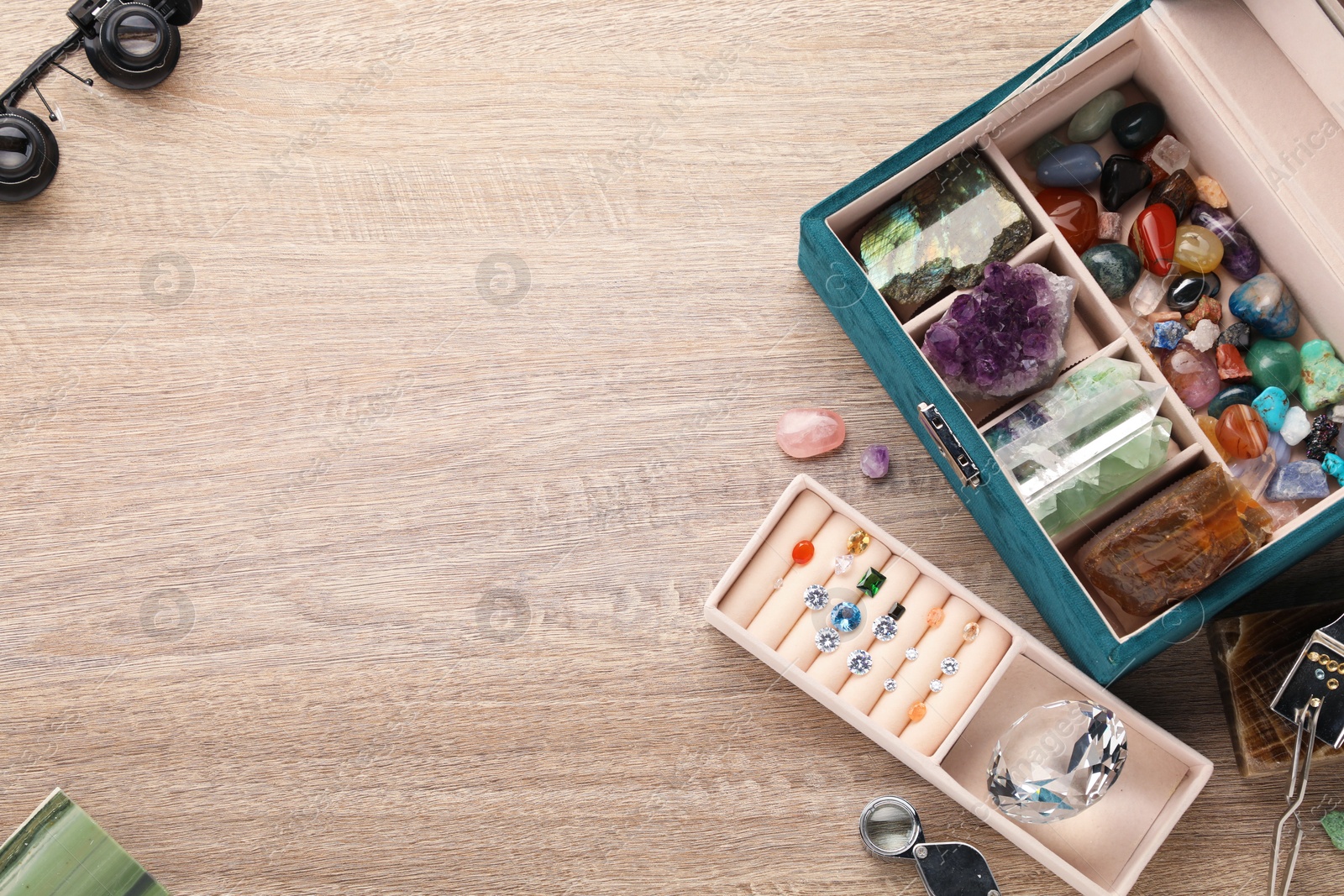 Photo of Box with beautiful gemstones and jeweler's tools on wooden table, above view. Space for text