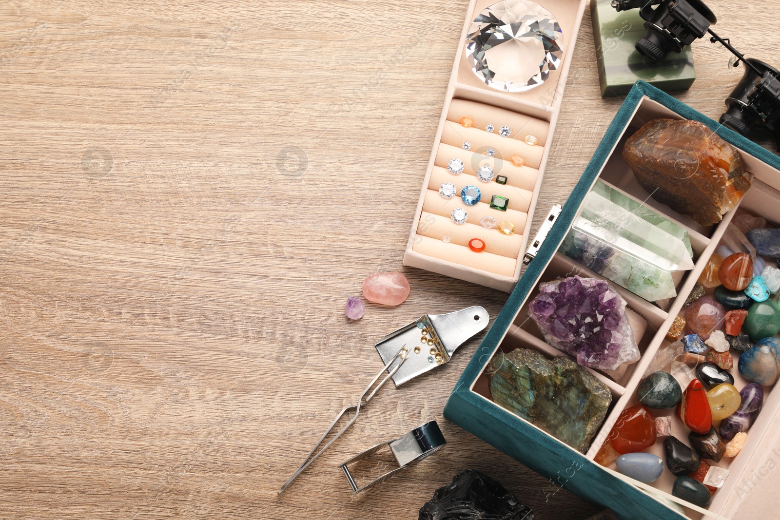 Photo of Box with beautiful gemstones and jeweler's tools on wooden table, above view. Space for text